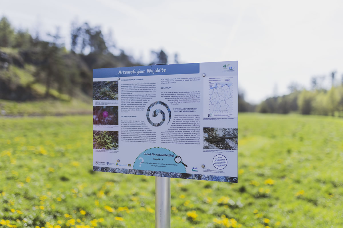 Am Perlenradweg auf der Brücke über die Schwesnitz informiert ein Schild über die Artenvielfalt auf der Wojaleite – mit Blick auf die imposante Felswand (Foto: Landkreis Hof).